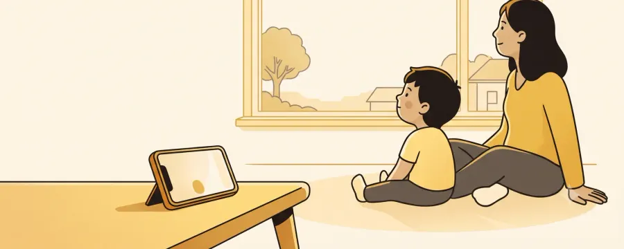A young child and a parent sitting together on the floor, looking out of a big window at a bird on a wire and trees in the distance, with a phone left propped on a stand on a low table nearby.