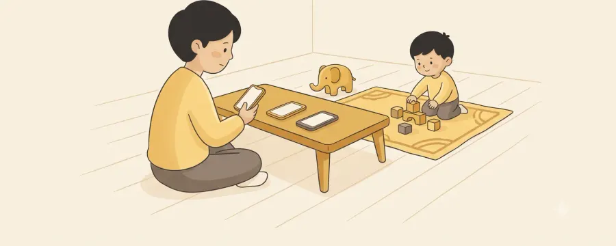 A parent sitting on the floor at a low table holding one phone, with two more phones lying flat on the table beside them, while a young child plays with wooden blocks on a rug nearby.