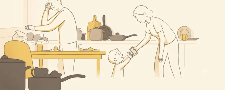 A busy kitchen in the early evening: one parent on a phone call by the counter, the other bending down to hand a phone to a small child.