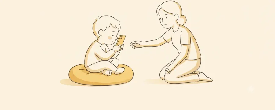 A small child sitting cross-legged on a floor cushion holding a phone right up close to their face, while a parent kneels nearby and reaches out gently to move it back.